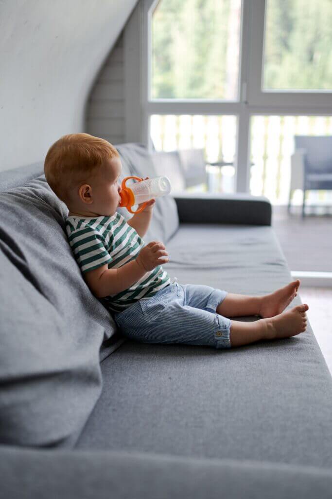 a little boy drinks from a zippy cup while sitting on the couch a little boy drinks from a zippy cup while sitting on the couch