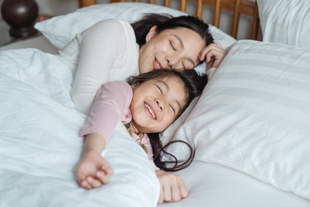 Cheerful mother and daughter resting in bed having defeated depleted mother syndrome